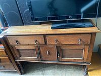 Front view of the wood dresser showing three drawers and two cabinet doors with metal handles. Surface appears scratched and worn.