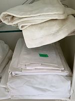 Folded off-white and white bed linens stacked on a surface, some labeled 'king'