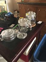 Photo of the group set on a dark surface including the glass teapot, percolators, lids, and extra parts.