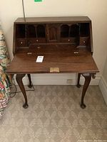 Front view of vintage mahogany desk showing fold-down writing surface, internal storage compartments including drawers, dividers, and a central cabinet.