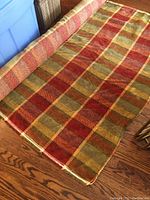 Remnant roll of plaid upholstery fabric laid out on floor showing colors and pattern