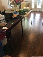 Photo showing dark wood folding card table from a side angle with some household items on top. The table appears sturdy with a smooth wood surface.