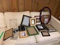 Various frames of differing sizes and styles arranged on a light-colored couch, highlighting the assortment and vintage oval frame with curved glass.