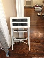Photo of a small white metal step stool with two black non-slip grip strips on top platform seen folded up against a doorway.