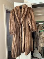 Full front view of medium-length mink fur coat hung on hanger