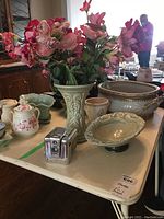 Wide view of all items on a table including ceramic vase with pink faux flowers, decorative bowl, jewelry box shaped like a vintage camera, and other ceramics around.