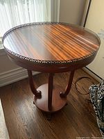 Full view of round wooden side table showing metal trim and water stains on top surface with three curved legs and base.