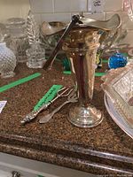 Overall view of sterling silver vase with swing handle and two ornate condiment forks on countertop