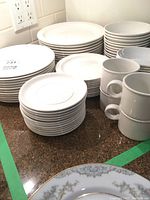 Stacks of plain white dinner, side and salad plates alongside mugs