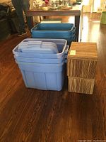 Photo showing stacked blue Rubbermaid bins with lids and two striped fabric bins on hardwood floor.