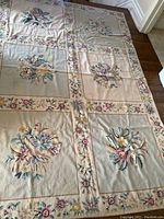 Full view of rectangular tapestry rug laid flat on floor showing floral panels and border pattern