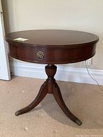 Front view of antique Duncan Phyfe style pedestal drum table showing round top and drawer with decorative brass ring pull.