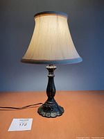 Front view of the antique style metal table lamp showing the decorative base, beige lampshade, and pull chain.
