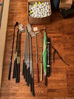 All golf clubs, two umbrellas, and box of balls arranged on wood floor