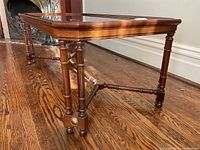 Side angle showing turned legs, cross-stretcher and brass accent medallion at foot
