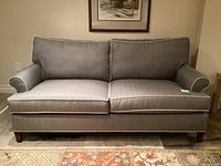 Front view of grey upholstered loveseat with white piping, two seat cushions and two back cushions under framed artwork