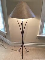 Full view of metal standing lamp with cone-shaped light gray shade and metal tripod base with curved legs.