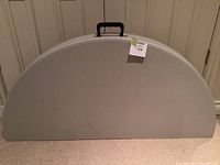 Folded table in closed position showing half-round shape and black handle for carrying.
