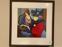 Front view of framed print showing stylized seated woman and table with flowers, artist signature and numbering visible on mat