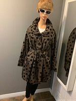 Mannequin wearing copper brown polyester coat with black velvet polka dots, double collar, buttoned front, belt at waist, and vintage mink hat against gray wall near mirror.