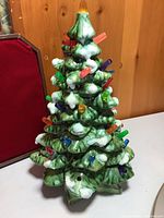 Front view of green ceramic Christmas tree with colored bulbs attached, standing 9 inches tall, showing snow-like accents and orange flame topper.