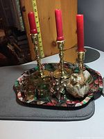 Three gold-toned Partylite candle holders each with red stub candles, beside other holiday items on a fabric surface.