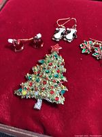 Christmas tree brooch and three distinct pairs of earrings displayed on red velvet.