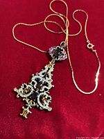 Photo shows the Christmas tree pendant on a 20-inch gold-tone chain against a red background. The pendant has amber and pinkish stones and a detailed filigree-like design.