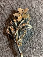 Front view of brooch showing shell flower with rhinestone stem and silver-toned leaves on gray fabric.