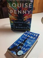 Photo showing both books, hardcover and paperback, titled 'The Madness of Crowds' and 'All the Devils Are Here' by Louise Penny