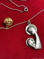 Photo showing the sterling silver Madonna with Child pendant on an 18-inch chain, alongside a small gold-toned guardian angel pin with rhinestone detail, all displayed on a red background.