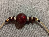 Close-up of central large red Murano glass bead surrounded by smaller red beads and rhinestone spacers on a gold-tone chain.