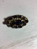 Oval vintage gold-toned brooch with central large red stone surrounded by smaller red stones, on light wooden surface.