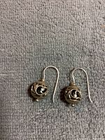 Pair of sterling silver earrings with hollow cutout balls on ear wires shown side by side on a gray textured fabric background.