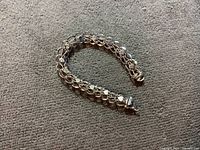 Full view of the folded chain bracelet on carpet, showing circular links with finer chain wrapped around each and the clasp.