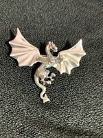 Close-up photo of sterling silver dragon pin with wings spread, showing detailed scales and claws on textured black background.