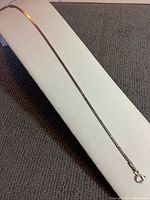 Full length view of the fine silver bracelet displayed on a white cushion, showing its length and thin linked chain.