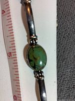 Close up of one green oval stone set in sterling silver with measuring tape in background showing size of stone and bracelet width.