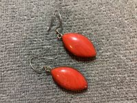 Pair of marquise-shaped orange-red stone earrings displayed on a grey textured surface, showing front and side views.