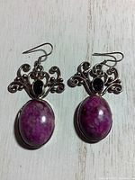 Pair of sterling silver earrings with pink marbled oval stone and garnet accent stones on a white wooden surface