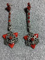 Close-up image showing the intricate silver and red stone star pattern and upper linear red stone design on earrings placed on fabric surface.