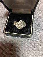 Front view of silver rhinestone ring in black velvet ring box showing wavy design with rhinestones.