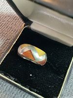 Sterling silver ring with yellow, brown, turquoise and orange stone inlays shown inside an open jewelry box on black velvet lining.