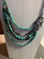 Close-up of the five strand necklace displaying turquoise and brown beads, silver chain, and leaf accent.