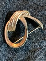 Front angle view of the vintage gold toned brooch shaped as a stylized letter 'Q', showing its smooth and textured metal design and pin back fastener.