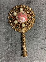 Front and decorative side of vintage pocket mirror showing detailed ornate gold-tone metal, pearls, and emerald-like stones with missing pieces