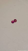 Pair of round pink-red rubies on white background, showing vibrant color and clarity