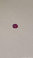 Oval cut natural ruby gemstone with pinkish red color and internal clarity enhancements visible on light reflection.