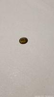 Photo of a small oval cut olive green orange tourmaline gemstone on a white background showing its color and size.
