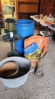 Photo of blue barrel, two green bird feeders, metal wash basin with wooden bucket inside, and basket with tarps and yellow rope